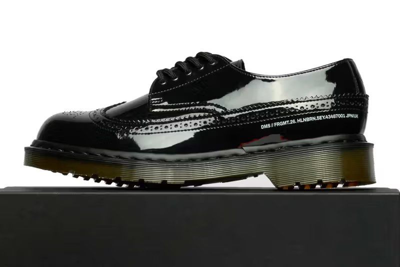 Fragment Design x Dr. Martens Hollingborn brogue in black patent leather, showing five-hole wingtip construction with tonal black hardware