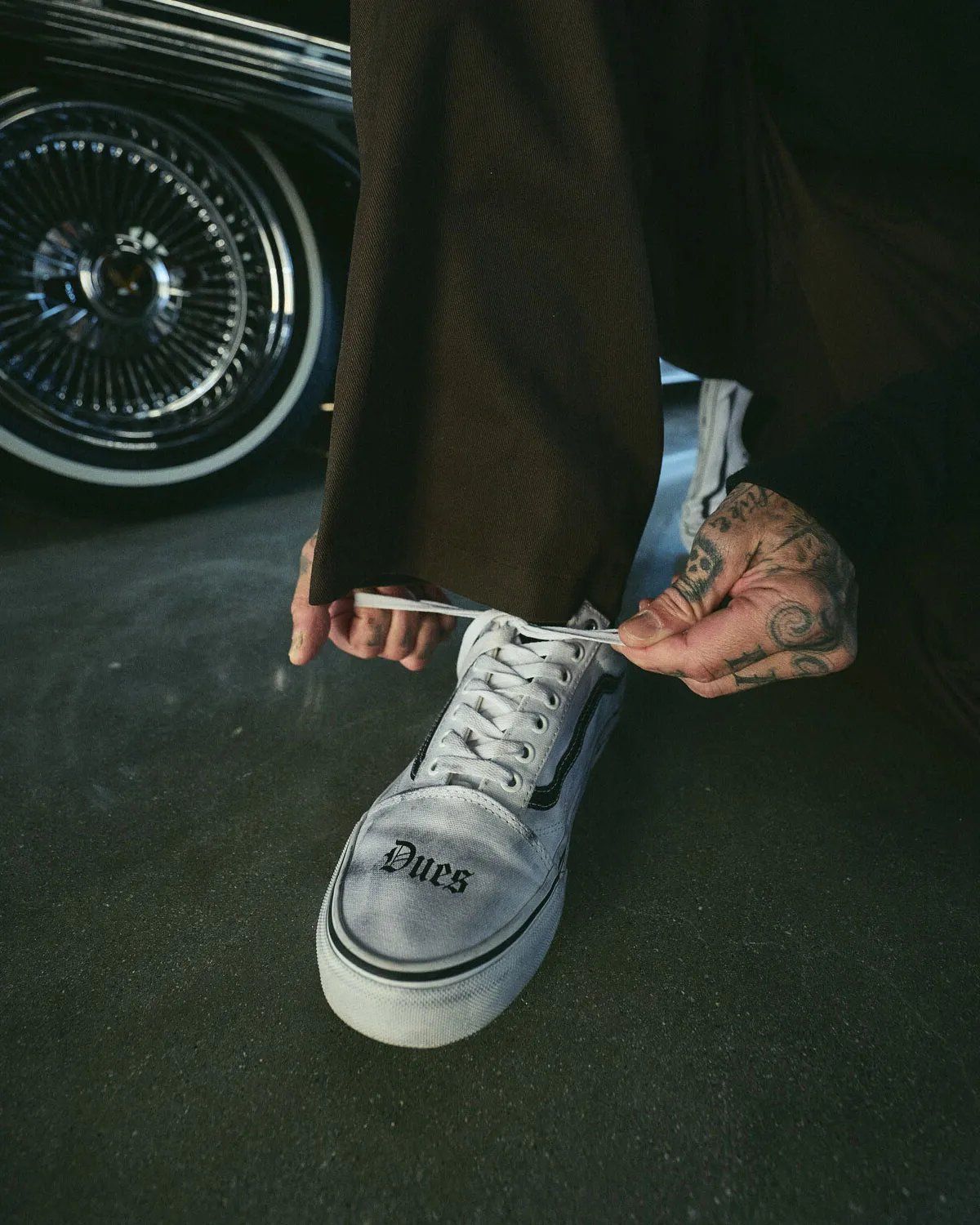 White Vans Old Skool with 'Dues Paid' text across toe box and barbed wire sidewall graphics from Travis Barker collaboration