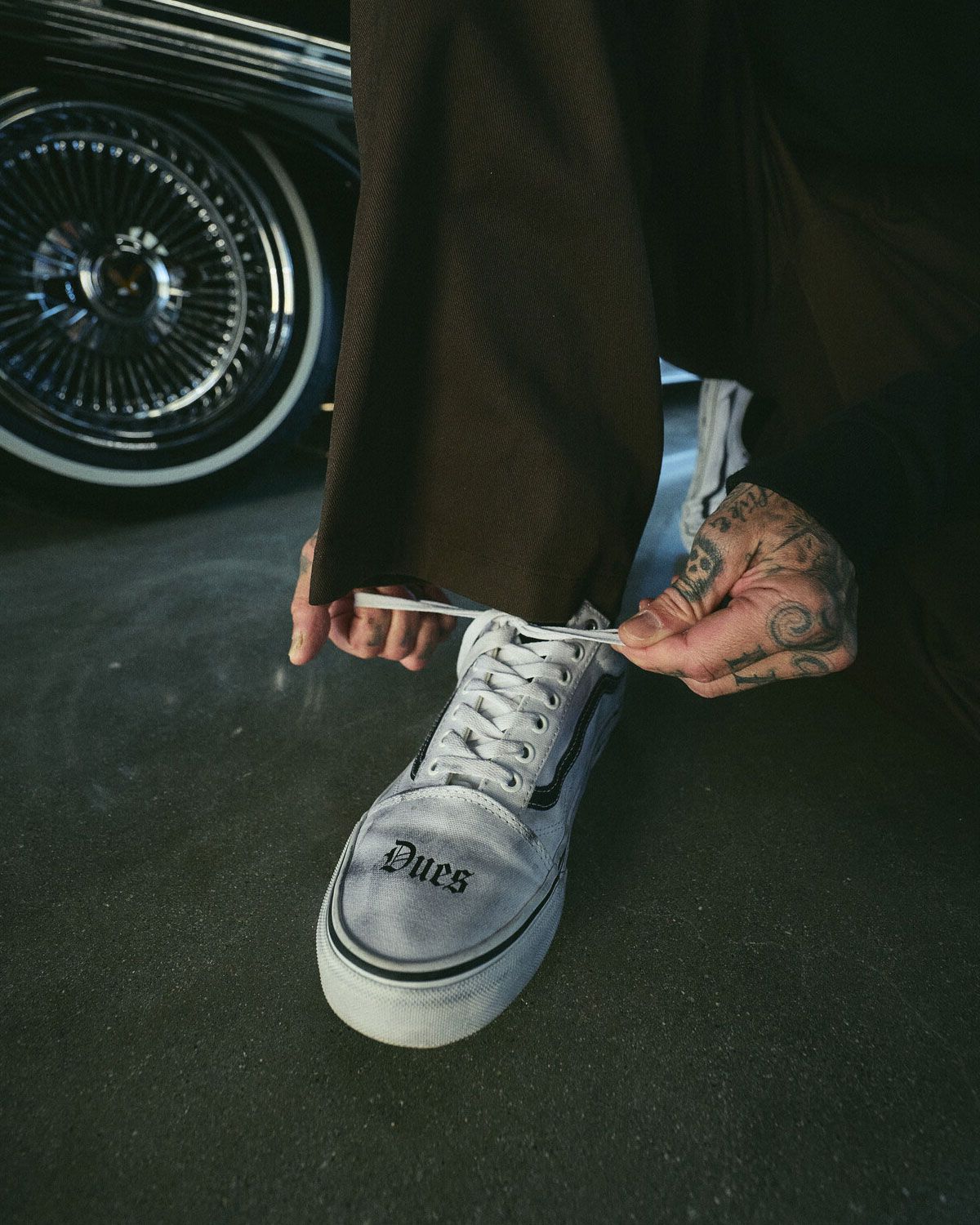 White Vans Old Skool with 'Dues Paid' text across toe box and barbed wire sidewall graphics from Travis Barker collaboration