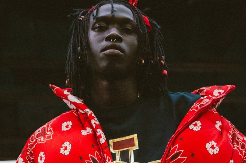 Peezy wears Denim Tears x Billionaire Boys Club collaboration pieces including chunky knit cardigan with red, black, and green striping on New York City street