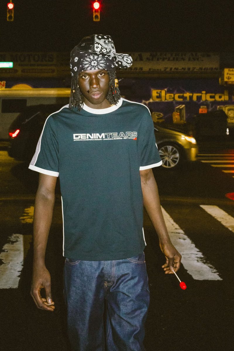 Peezy wears Denim Tears x Billionaire Boys Club collaboration pieces including chunky knit cardigan with red, black, and green striping on New York City street - detail view 3