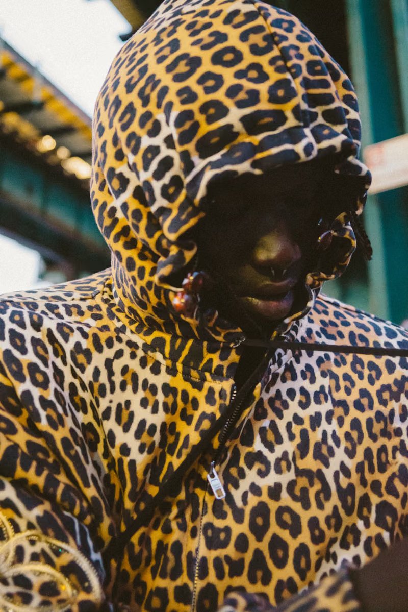 Peezy wears Denim Tears x Billionaire Boys Club collaboration pieces including chunky knit cardigan with red, black, and green striping on New York City street - detail view 4