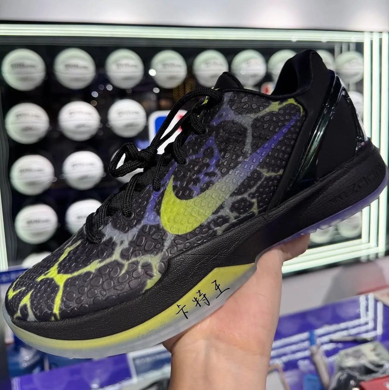 Nike Kobe 6 Protro 'Coals' in black with Venom Green and Purple Venom accents, shown in-hand with scaled upper and translucent outsole - detail view 2